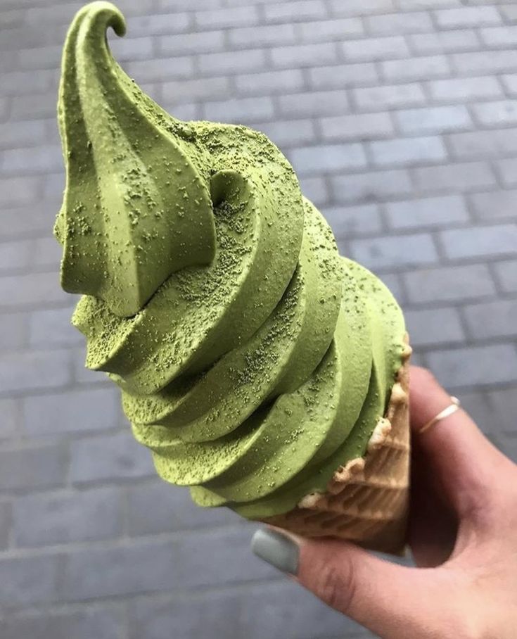 a hand holding an ice cream cone with green topping