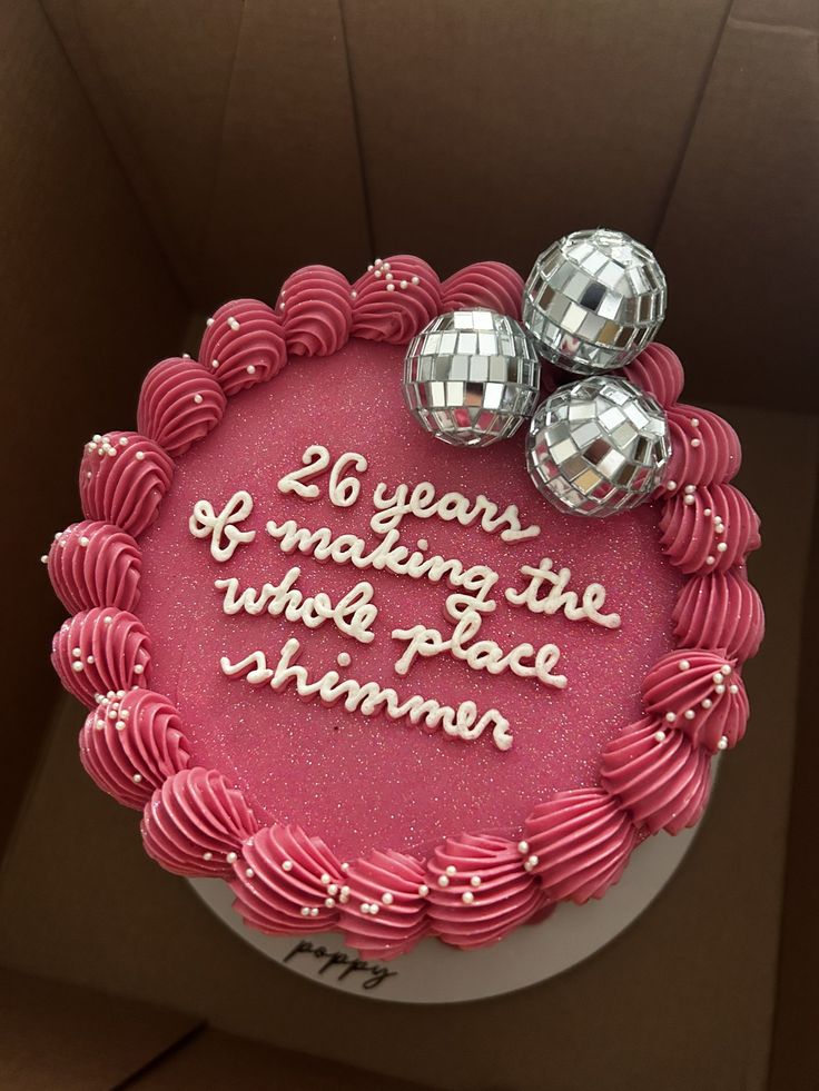 a birthday cake with pink frosting and two silver disco balls on top that says, 20 years of making the whole place shiner