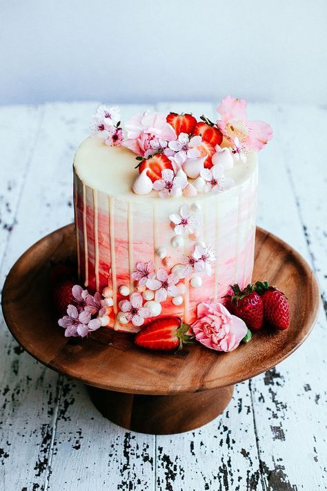 a white cake with strawberries and flowers on a wooden plate next to a knife