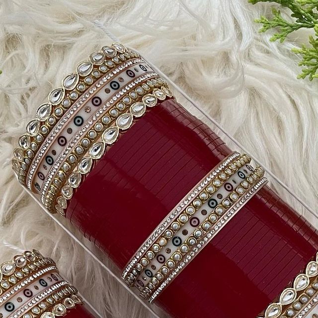 two red and gold bracelets sitting on top of a white fur covered floor next to flowers