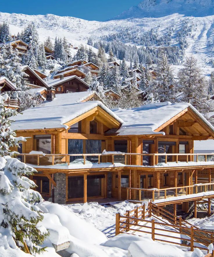 a large wooden house surrounded by snow covered trees and mountain range in the back ground