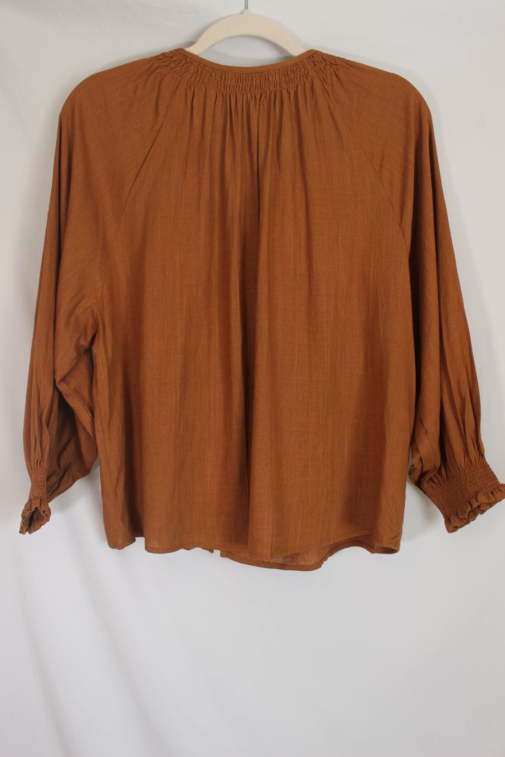 Simple and feminine caramel blouse with drop shoulder, front buttons, and smocked collar and cuffs details & fit: fits true to size. 70% viscose, 30% linen measurements: small: bust 44"/ waist 44"/ length 22" medium: bust 46"/ waist 46"/ length 23" large: bust 48"/ waist 48"/ length 24" model details: model is 5'7" and wearing size medium Billowy Long Sleeve Top With Smocked Cuffs, Spring Button-up Tops With Gathered Sleeves, Spring Button-up Blouse With Smocked Cuffs, Spring Blouse With Smocked Cuffs And Relaxed Fit, Fall Peasant Top With Blouson Sleeves For Daywear, Chic Brown Tops For Daywear, Relaxed Fit Button-up Tops With Gathered Sleeves, Relaxed Fit Tops With Gathered Sleeves And Button-up, Brown Relaxed Fit Blouse For Summer