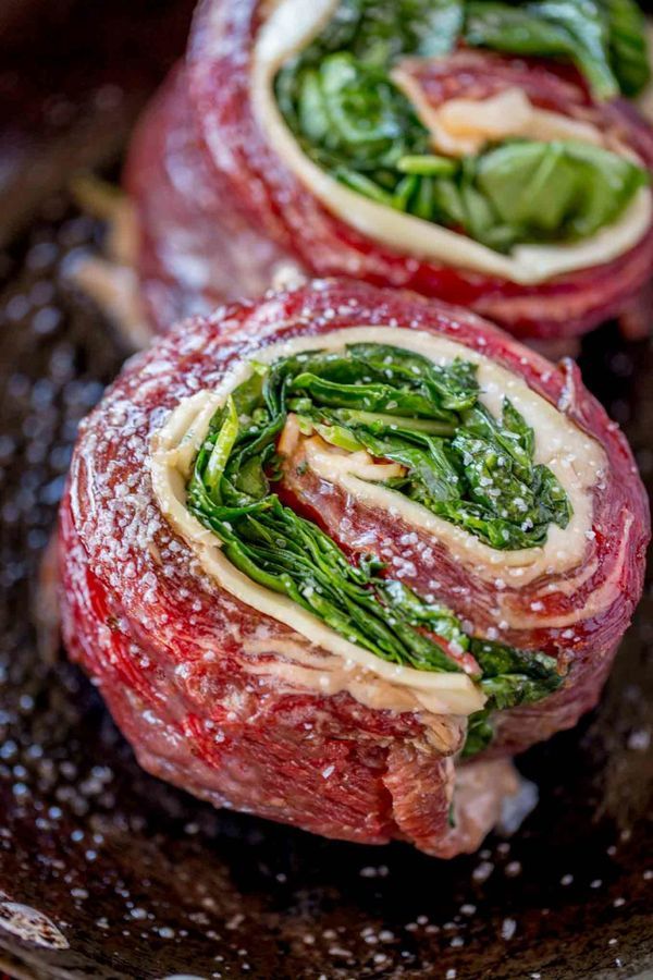 two raw meats with spinach and cheese on them in a black plate, ready to be cooked