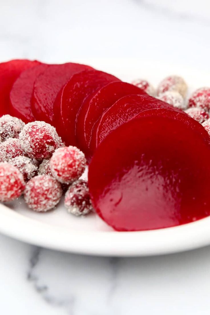 a white plate topped with red fruit covered in powdered sugar