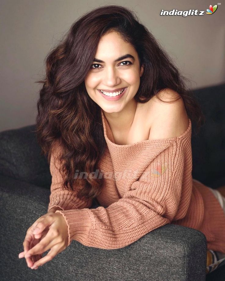 a woman sitting on top of a couch wearing a sweater and smiling at the camera