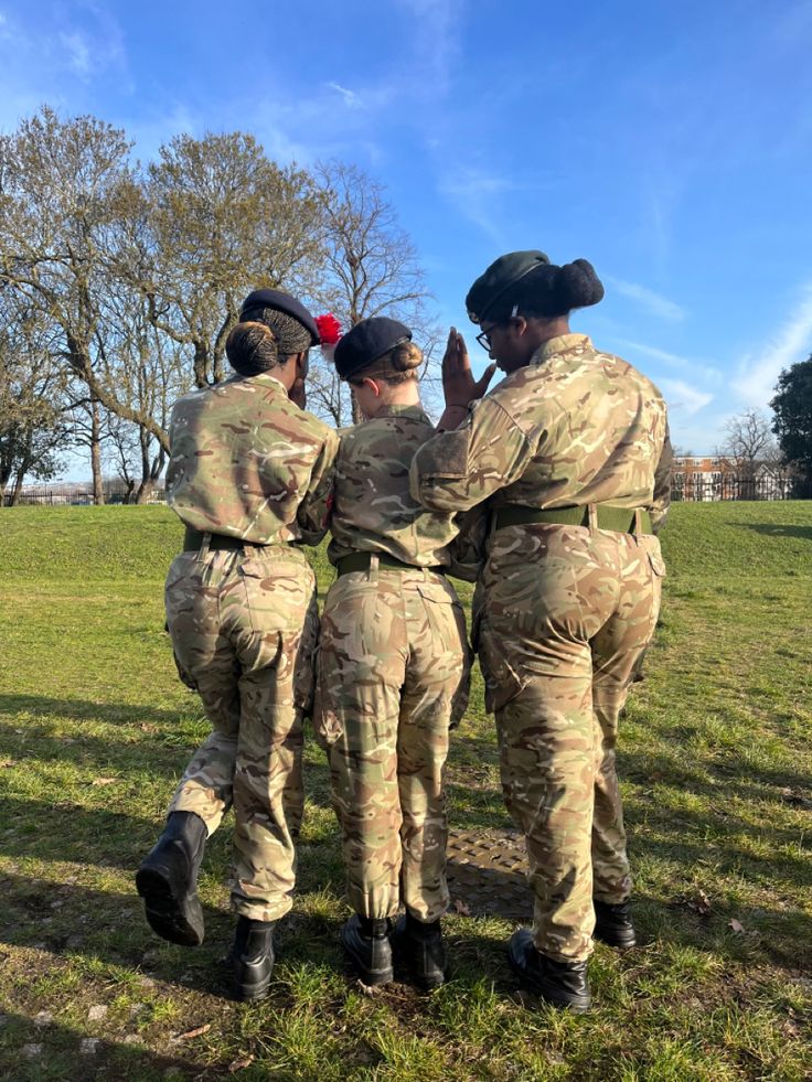 three soldiers are standing in a circle and talking to each other on the grass with trees in the background