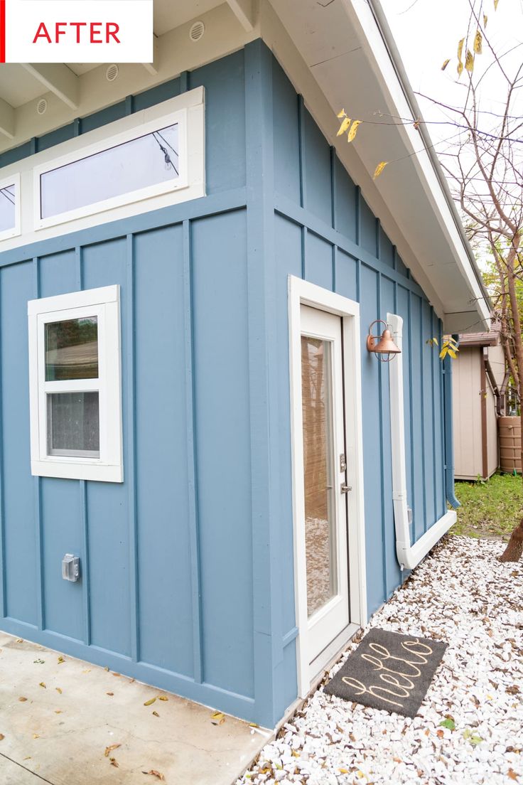 a small blue house with white trim and windows on the outside, next to a black door