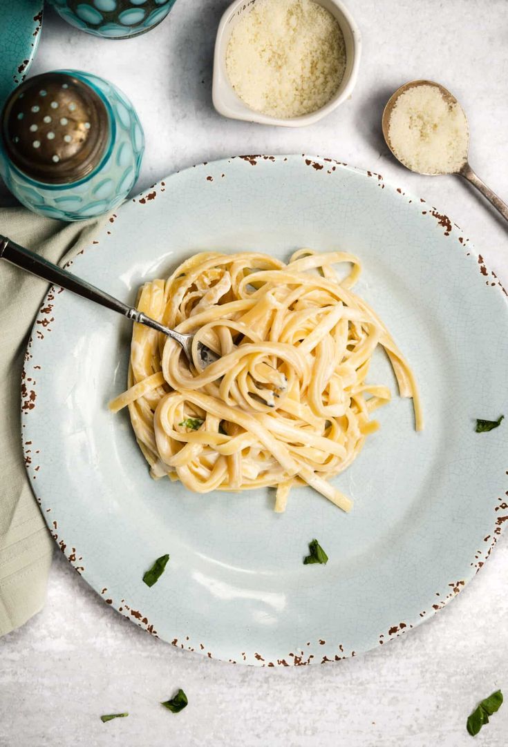 a white plate topped with pasta and parmesan cheese next to two spoons