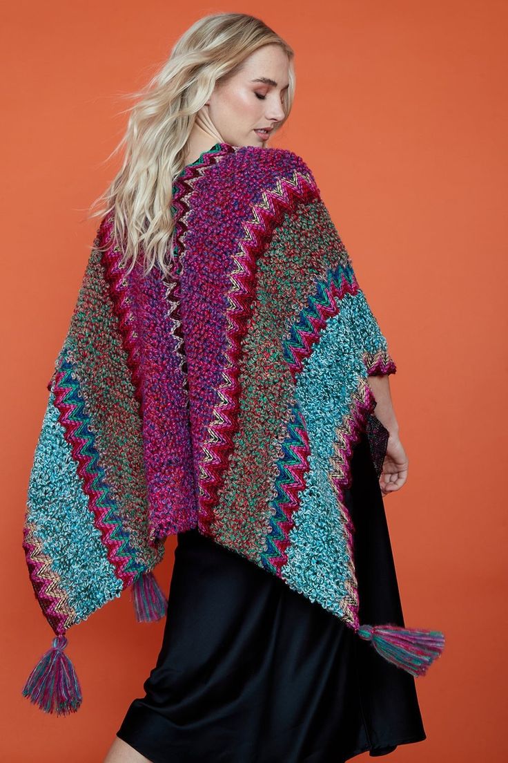 a woman wearing a multicolored crocheted shawl with tassels