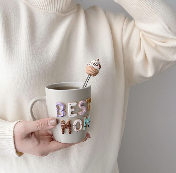 a woman holding a coffee mug with the words best mom on it and a cupcake in her hand