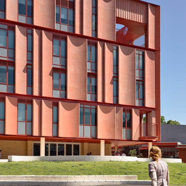 a woman is walking in front of an orange building with many windows and balconies