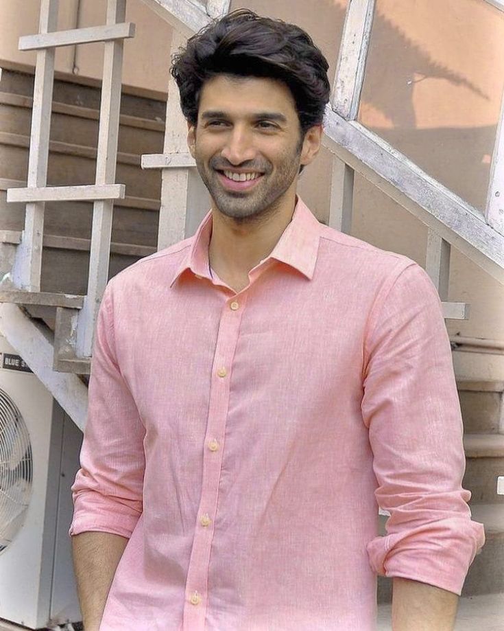 a man is standing in front of some stairs smiling at the camera with his hands in his pockets