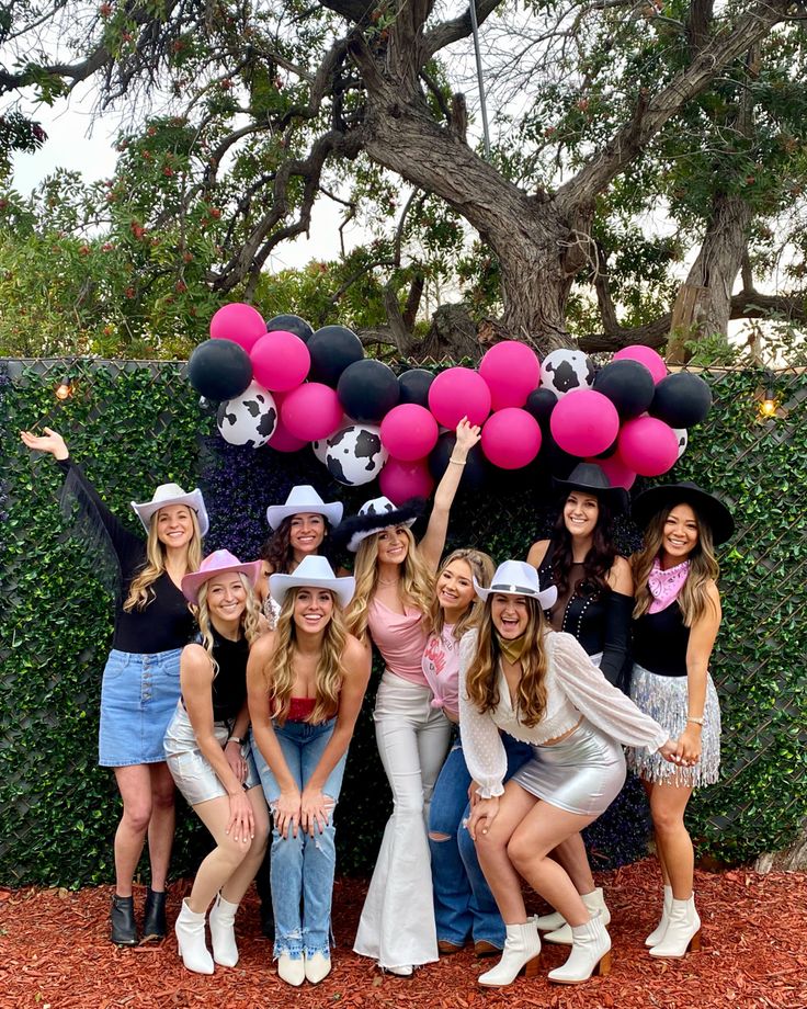 a group of women standing next to each other in front of a wall with pink and black balloons