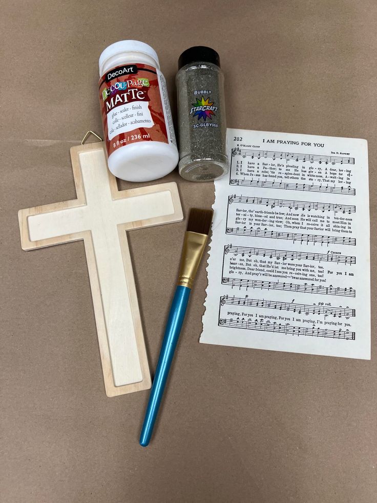 the cross is next to some paint and a brush on top of sheet music paper