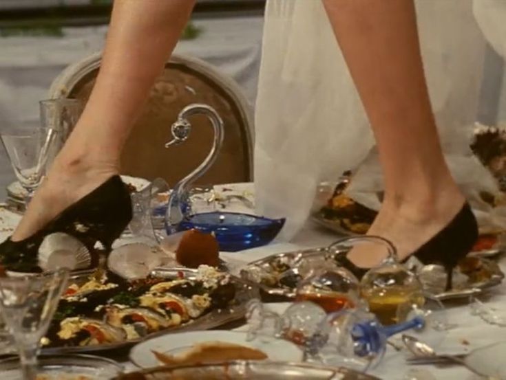 two women in high heels are standing over a table full of dishes and wine glasses