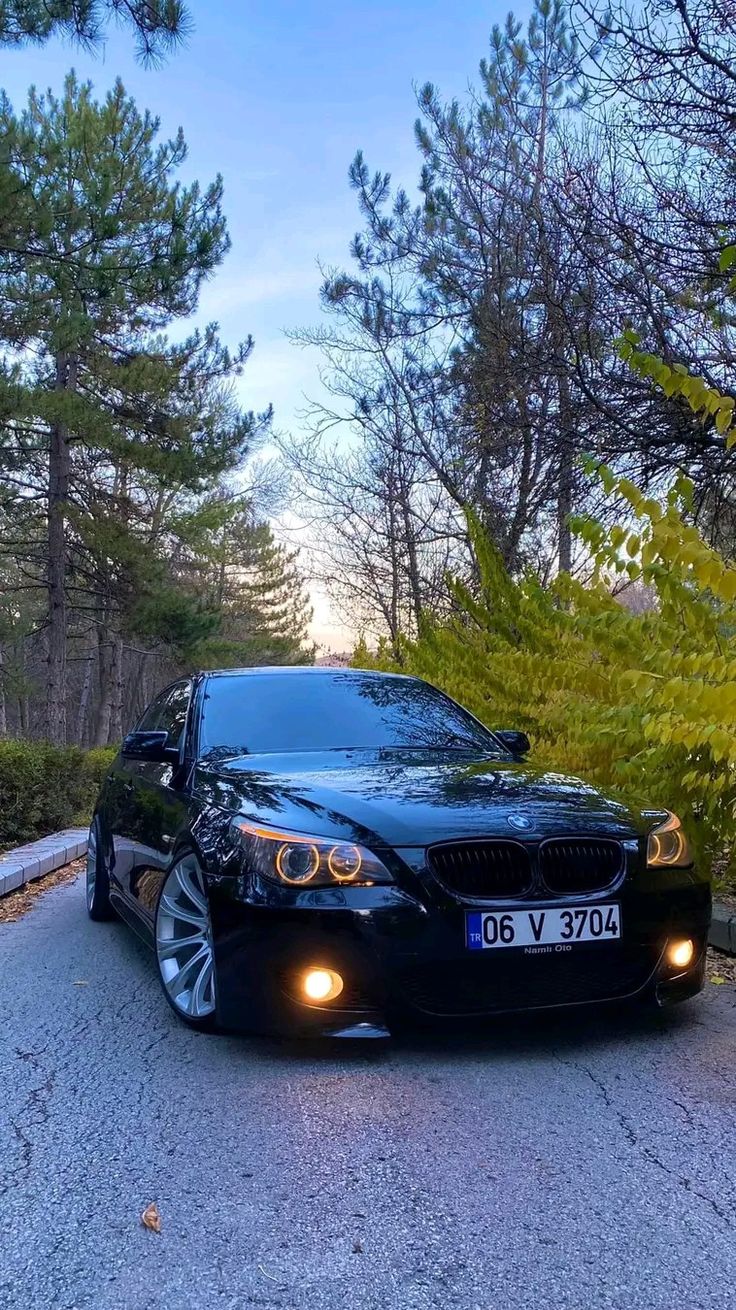 a black car is parked on the side of the road near some trees and bushes