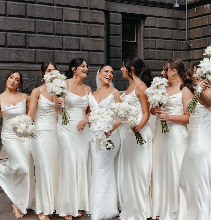 a group of women in white dresses standing next to each other holding bouquets and flowers