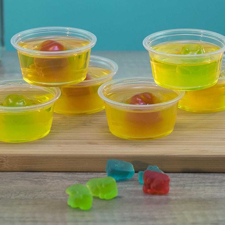 four plastic bowls filled with gummy bears on top of a cutting board next to jelly beans