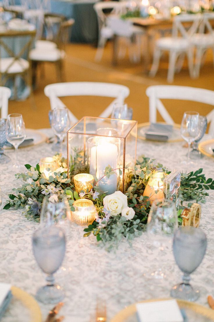 the centerpiece is surrounded by candles and greenery, along with other tables set for dinner