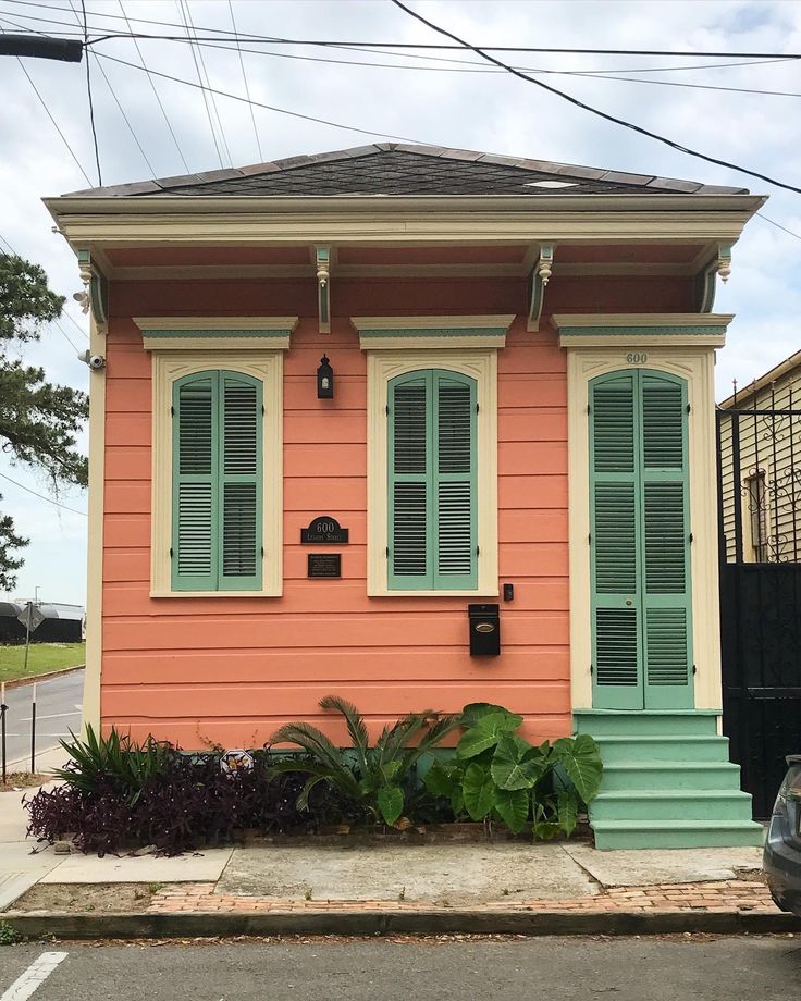 an orange house with green shutters on the front and side windows is next to a black car