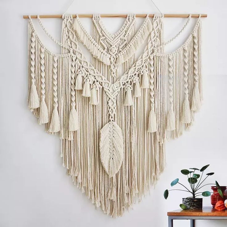 a wall hanging with macrame and tassels on top of it next to a potted plant