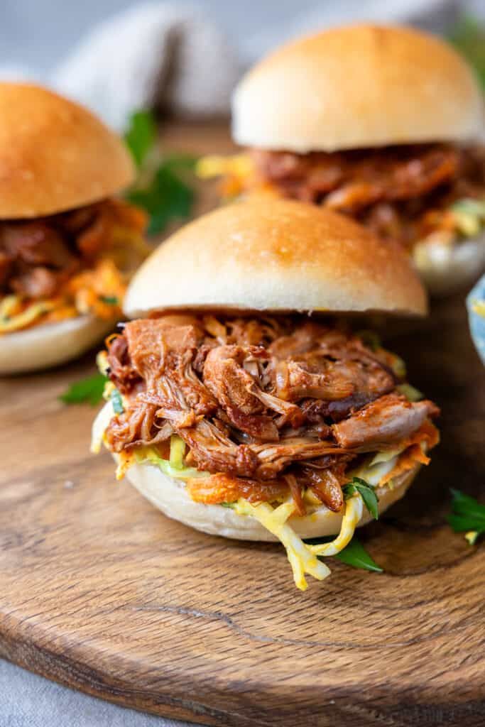 three pulled pork sandwiches sitting on top of a wooden cutting board