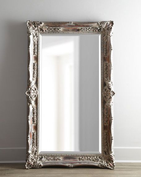 an ornate silver framed mirror on the floor in front of a white wall and wooden floor