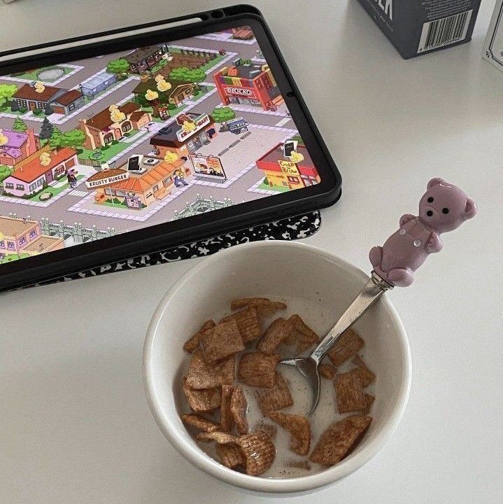 a bowl of cereal with a spoon in it next to a tablet and a toy bear