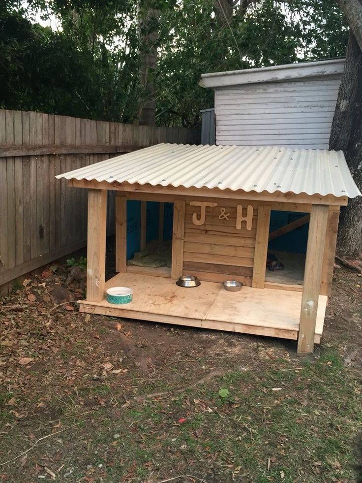 a dog house made out of pallet wood with a metal roof and two bowls on the outside