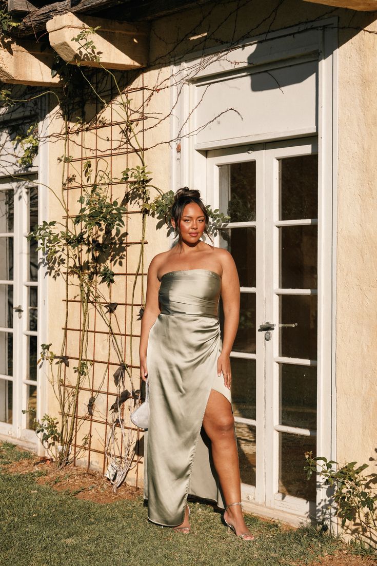 a woman standing in front of a house wearing a silver dress and holding a white purse