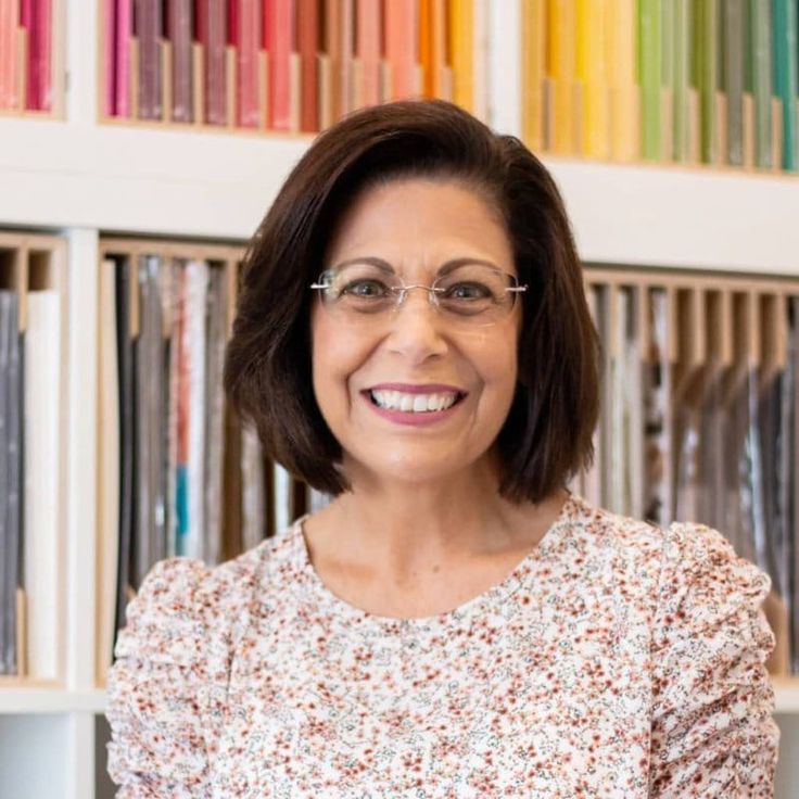 a woman with glasses standing in front of bookshelves