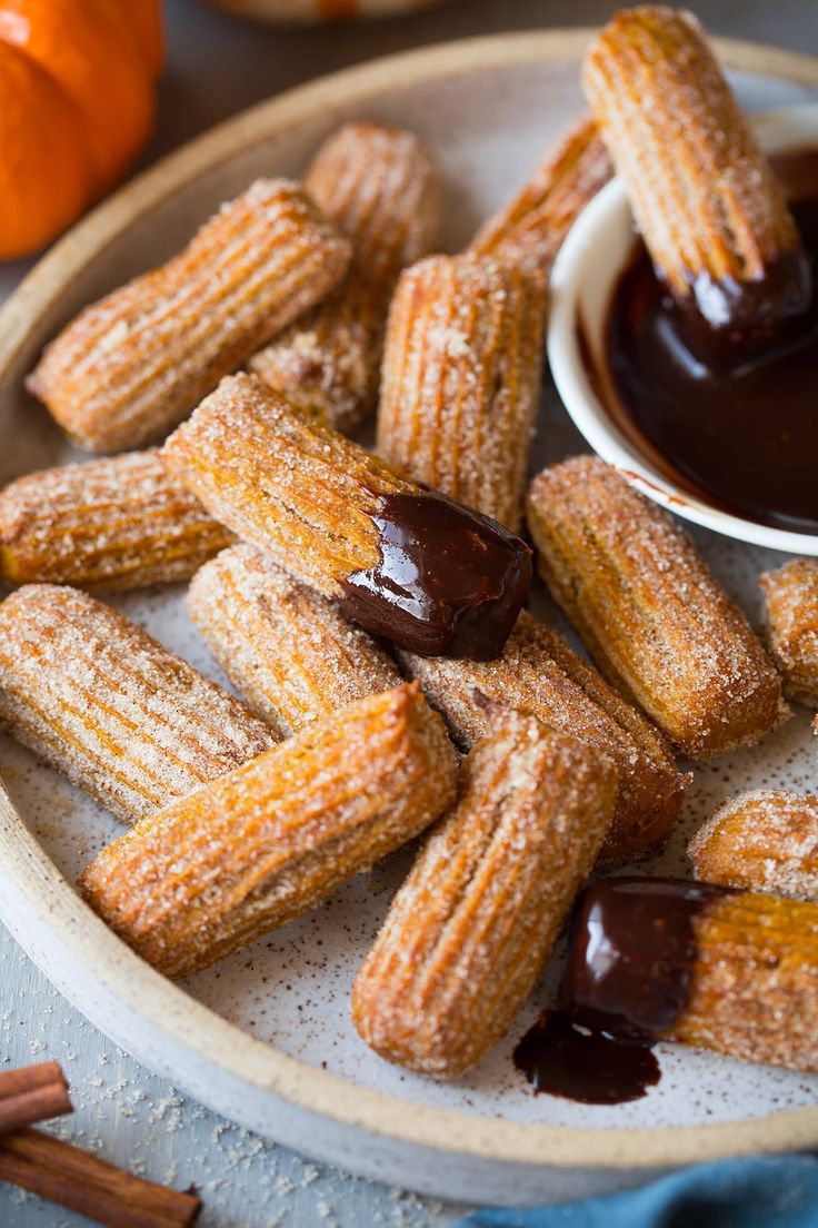 powdered sugar coated donuts on a plate with dipping sauce in the background and an orange