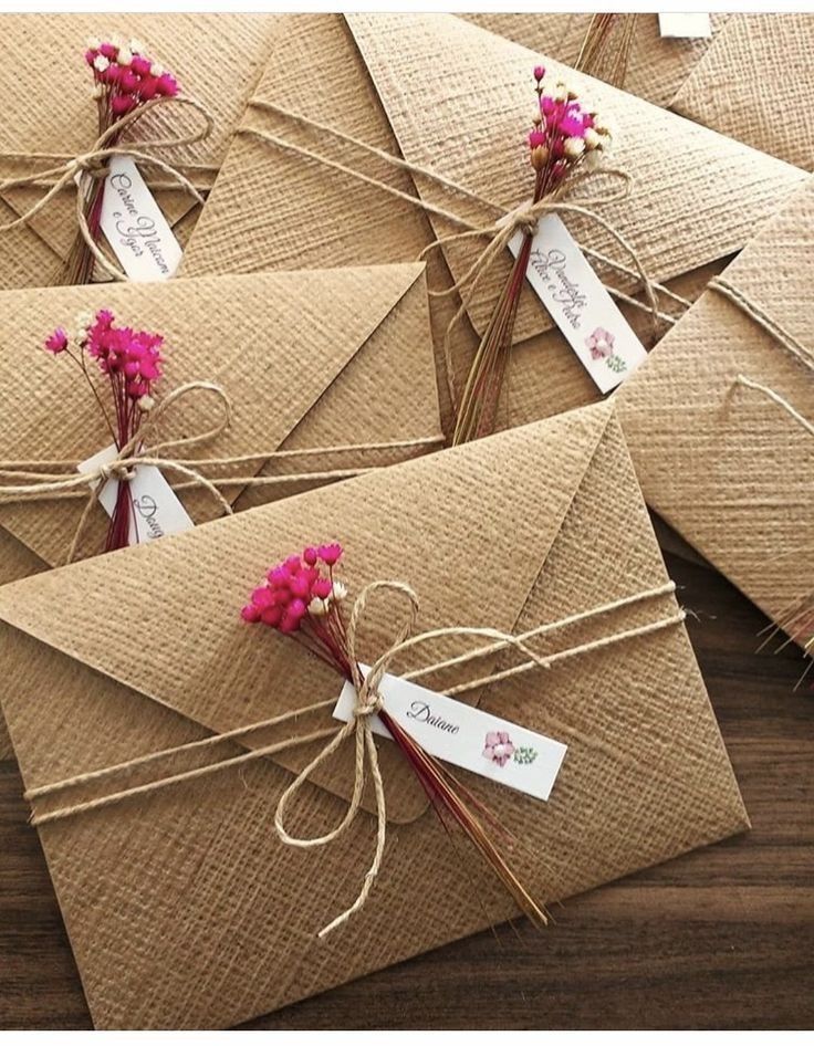 several envelopes tied together with twine and pink flowers are shown on a table