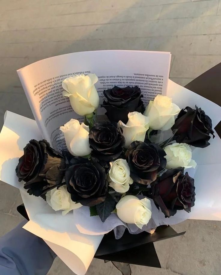 a bouquet of white and black roses on top of an open book in someone's hand