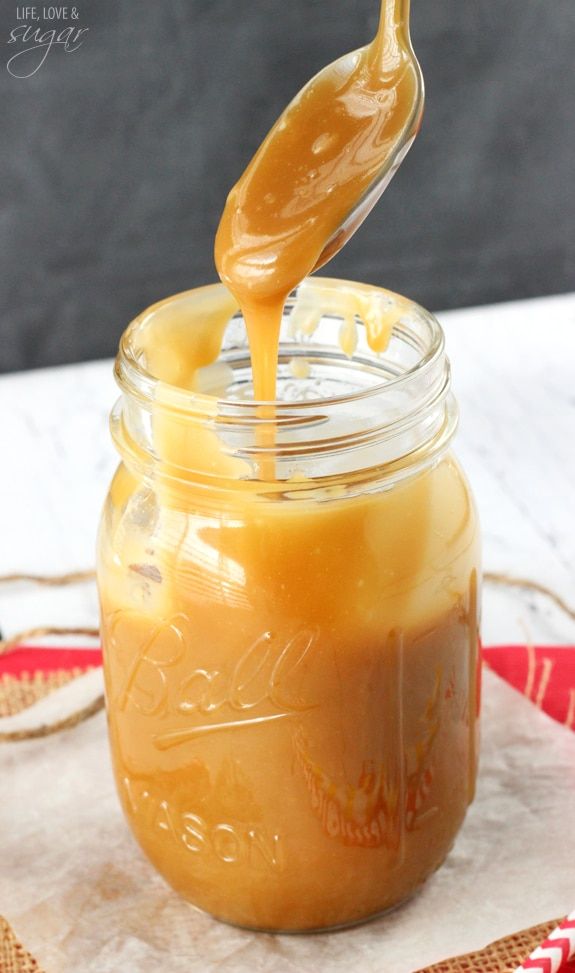 a jar filled with caramel sauce on top of a wooden table next to a red and white napkin