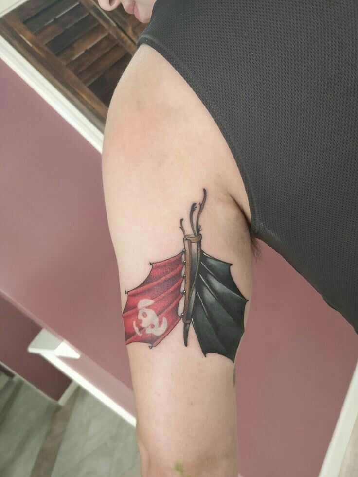 a woman with a tattoo on her arm holding onto a red and black dragon wing