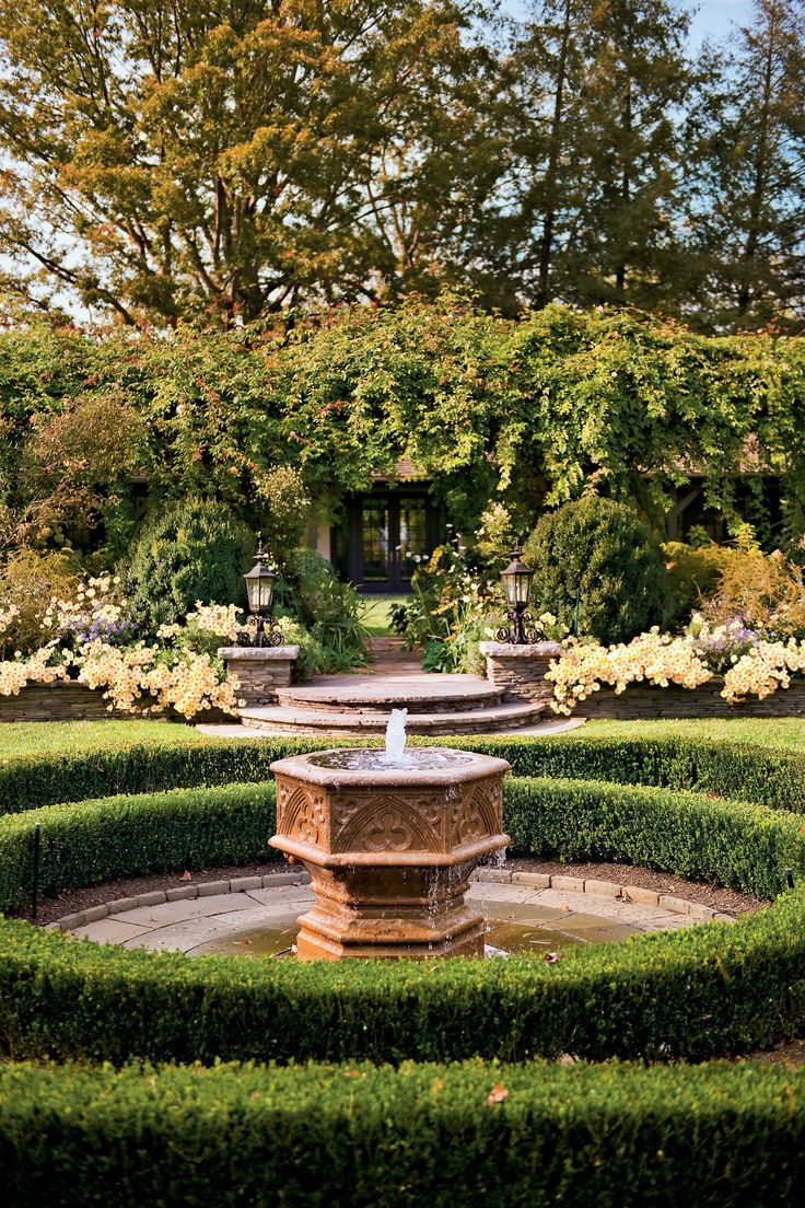 a fountain surrounded by hedges in the middle of a garden