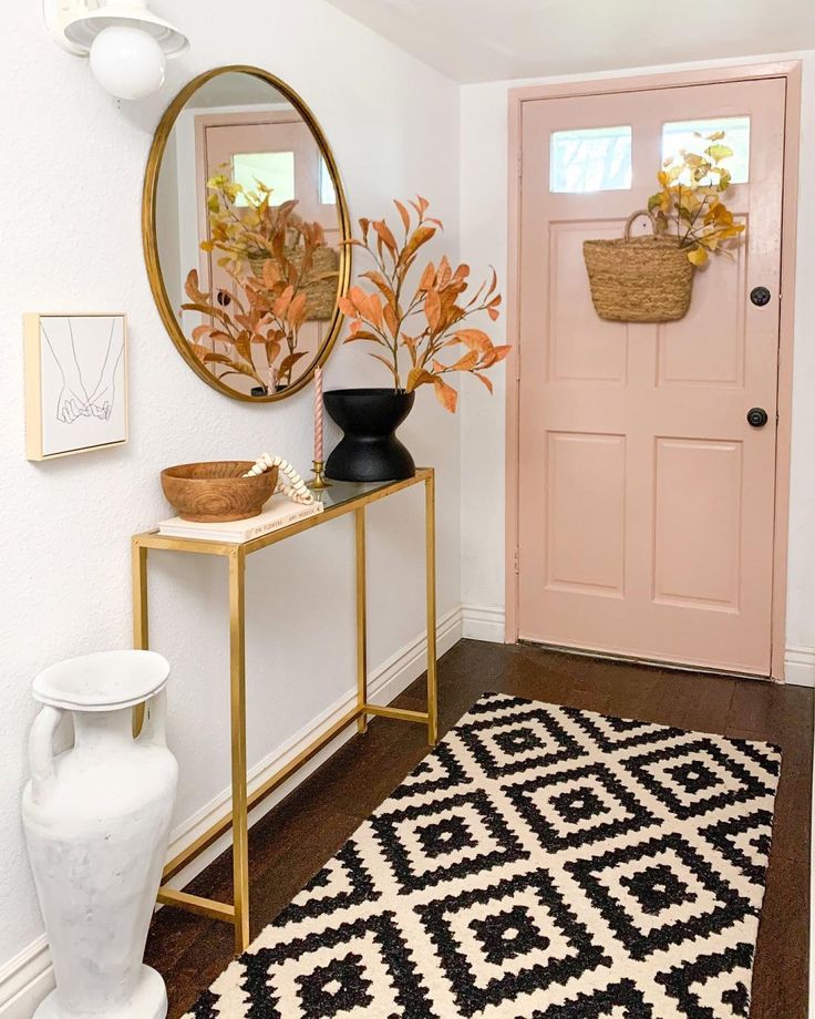 a hallway with a pink door, black and white rug, gold framed mirror and potted plant