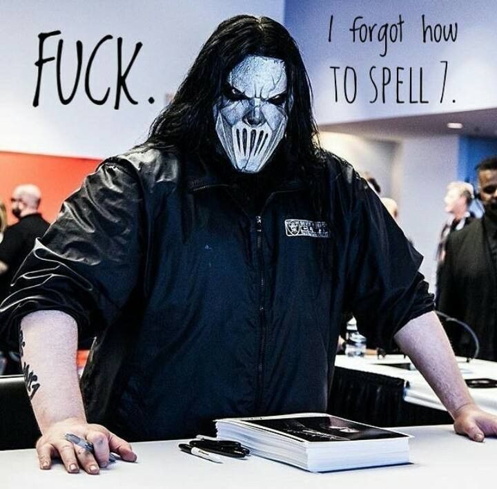 a man with long hair wearing a black jacket and white face paint standing in front of a table