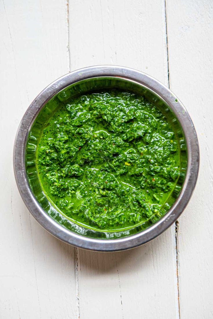 a metal bowl filled with green food on top of a white table