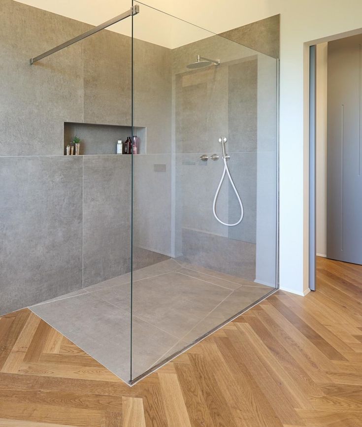 a bathroom with a glass shower door and wooden flooring, along with an open shelving unit on the wall