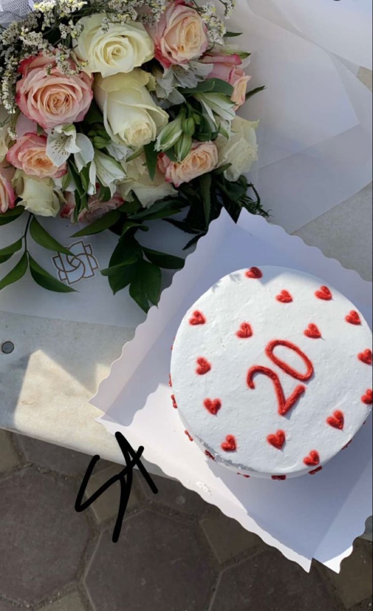 a white cake sitting on top of a table next to a bouquet of roses and flowers