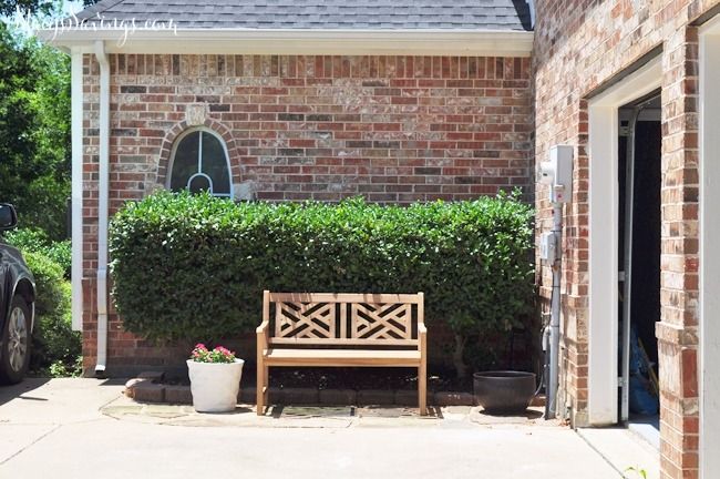 a wooden bench sitting in front of a brick building next to a tree and bushes