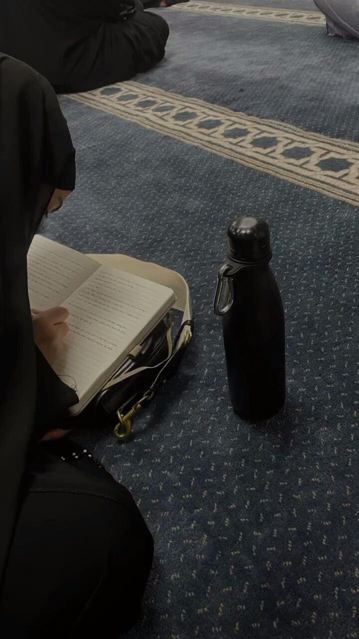 a person sitting on the floor with an open book in front of them and a bottle next to it