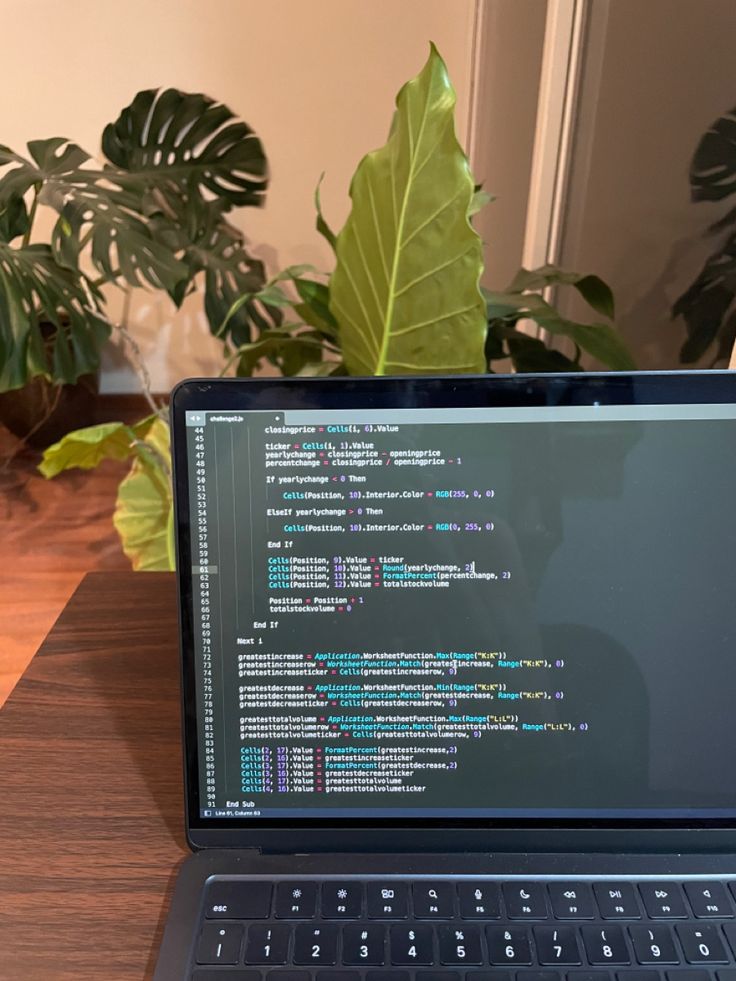 an open laptop computer sitting on top of a wooden table next to a potted plant