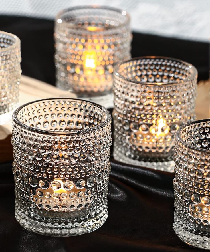 four clear glass votives with lit candles in them on a black tablecloth