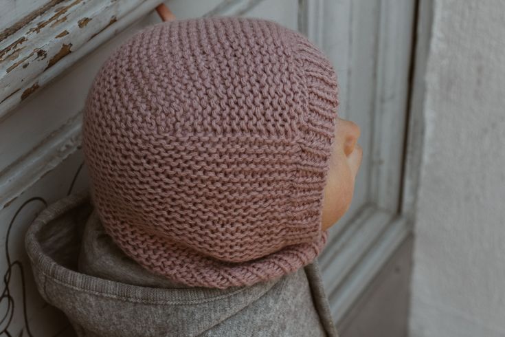 a small child wearing a pink knitted hat on top of a doorknob