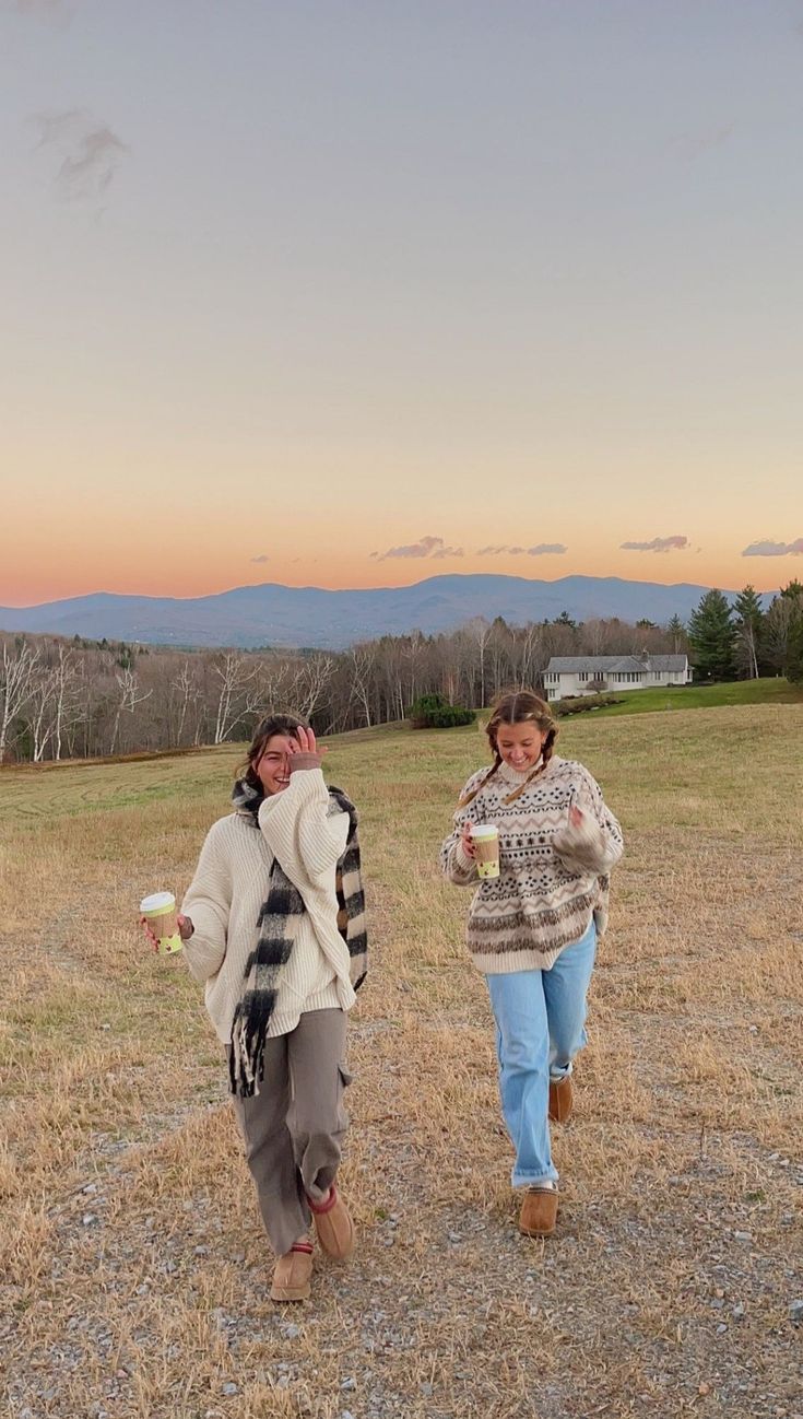 two women walking in a field at sunset, one holding a cup and the other carrying a frisbee