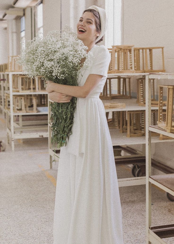 a woman in a white dress holding a bouquet of flowers and smiling at the camera