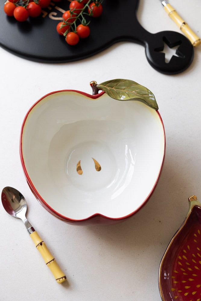 an apple shaped bowl with spoons on a table next to other kitchen utensils